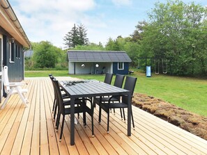 A wooden deck with a table and chairs, a small building, and a grassy area with trees. - 4 Star Holiday Home in Thyholm (Thyholm)