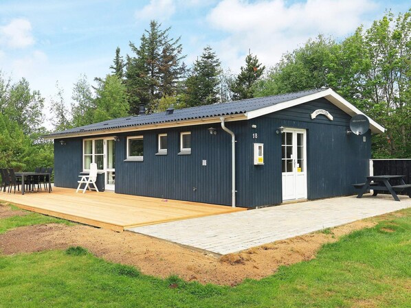 A small, dark blue building with a wooden deck, a white door, and a satellite dish. - 4 Star Holiday Home in Thyholm (Thyholm)