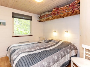 A bedroom with a bed, a window, a chair, and a wall-mounted shelf with folded blankets. - 4 Star Holiday Home in Thyholm (Thyholm)