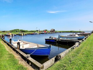 A calm waterway with boats docked along the banks, a grassy area, and a small building in the distance.