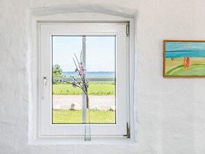 A room with a white door, a clear view of a beach, and a painting on the wall.