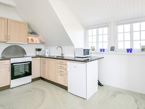 A modern kitchen with a built-in oven, microwave, and refrigerator, wooden cabinets, and a large window providing natural light.