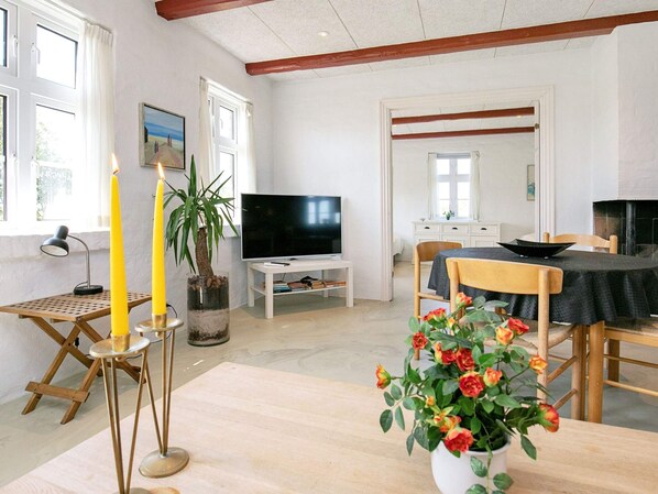 A room with a television, a dining table with chairs, a potted plant, and candles.