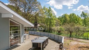 Une terrasse avec une table et des chaises, un espace salon abrité et une vue sur une maison et des arbres.