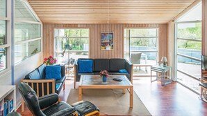 Un salon spacieux avec un plafond en bois, de grandes fenêtres, un canapé, une table basse et un téléviseur.