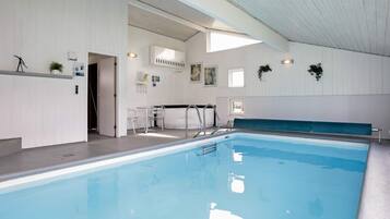 An indoor swimming pool with a clear view of the pool area, a seating area, and a reception desk.