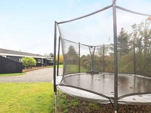 A trampoline with a safety net, set in a grassy area with a building in the background. - 5 Star Holiday Home in Hjorring (Hjørring)