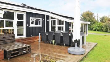 A modern outdoor seating area with a wooden deck, a white umbrella, and a tall white column.