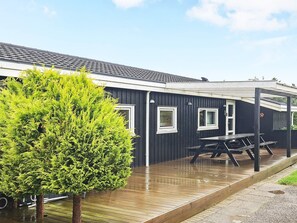 A modern building with a covered outdoor area, a wooden deck, and a small tree.