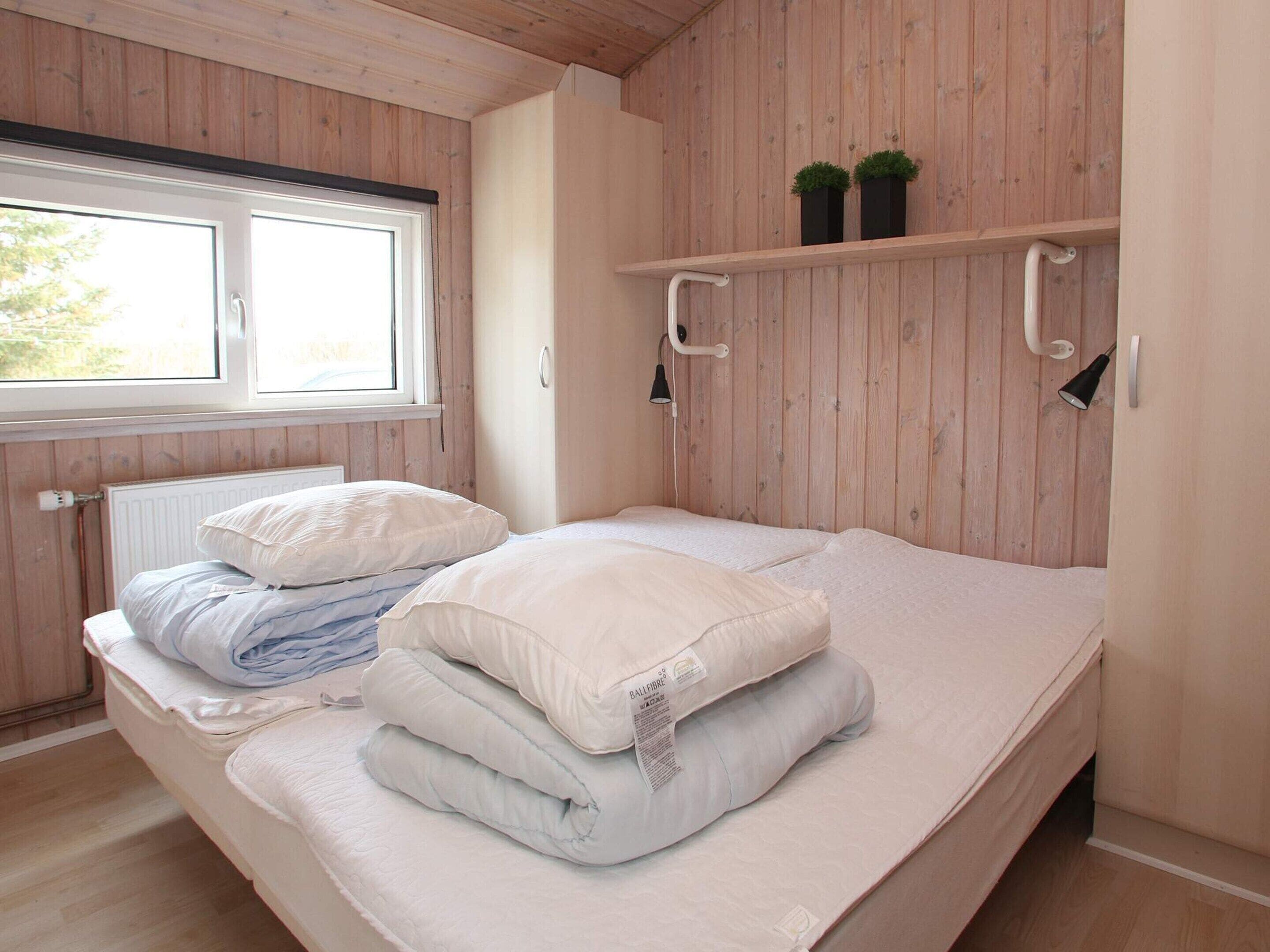 Un dormitorio con cama, almohadas, una ventana y paredes de madera.