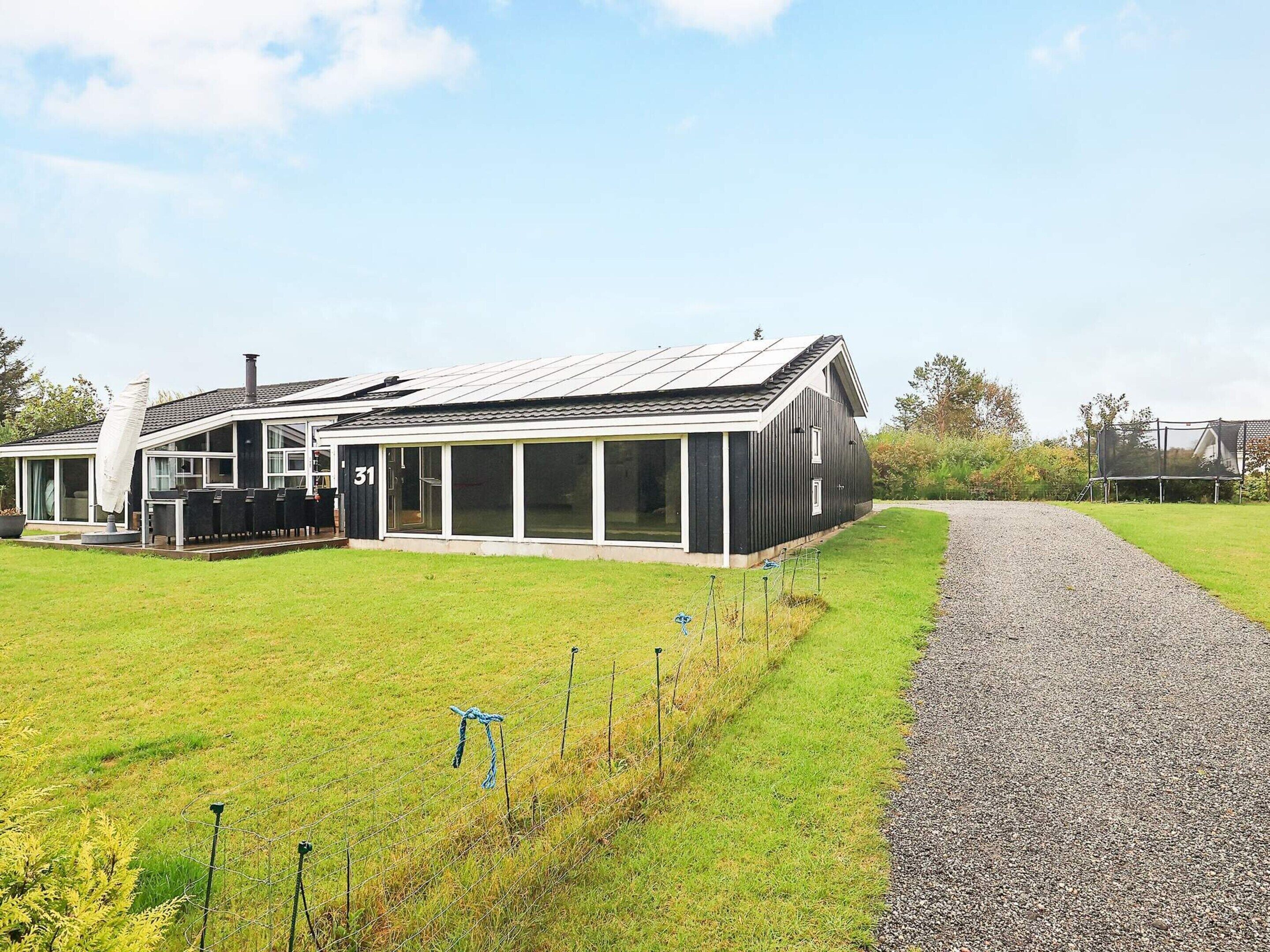 A modern house with a large glass extension, a gravel driveway, and a fenced garden area.