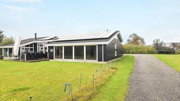 A modern house with a large glass extension, a gravel driveway, and a fenced garden area.