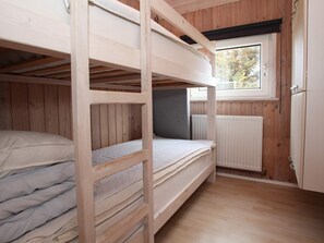 Une chambre avec un lit superposé, une fenêtre, des murs en bois et un radiateur.