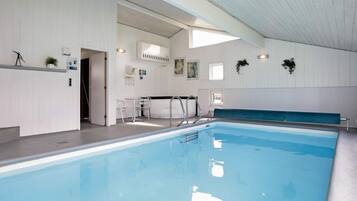 An indoor swimming pool with clear water, a seating area, and a reception desk.