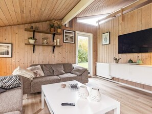 A cozy living room with a wooden ceiling, a sofa, a coffee table, and a television.