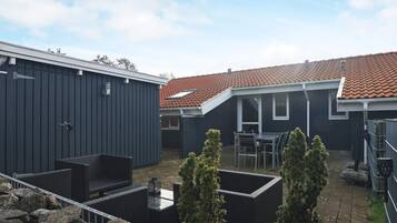 Un patio con zona de terraza, una pequeña mesa y sillas, y un edificio con techo de tejas.