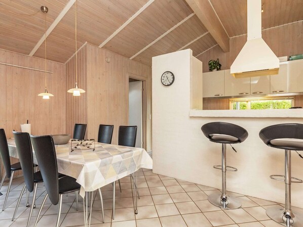 A dining area with a table and chairs, a kitchen area with a counter and stools, and a clock on the wall. - 4 Star Holiday Home in Humble (Sydlangeland)