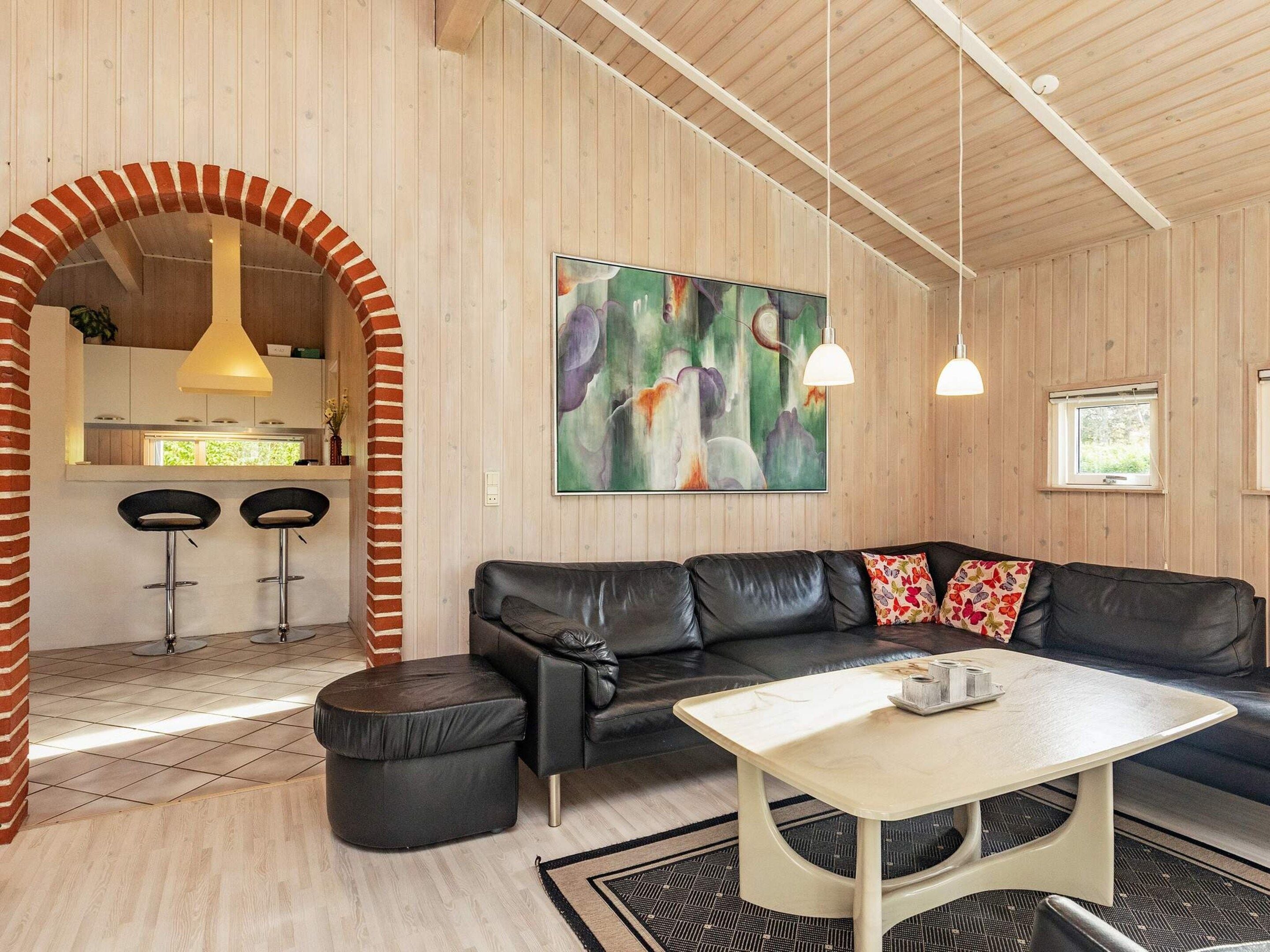En moderne stue med en sort lædersofa, et sofabord og et billede på væggen.