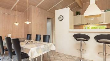 A dining area with a table and chairs, a kitchen area with a counter and stools, and a clock on the wall.
