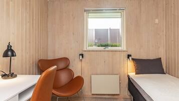 A compact room with a single bed, a desk, a chair, a window, and a radiator.