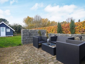 A patio area with wicker furniture, a small shed, and a hedge with autumn foliage.