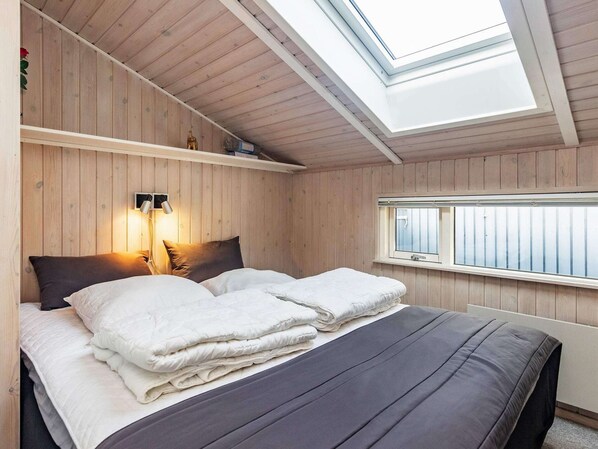 A room with a bed, a skylight, a window, and a wall-mounted light fixture.