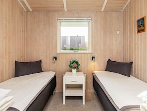 A room with two beds, a small table with a plant, a window with a view of buildings, and wall-mounted lights. - 4 Star Holiday Home in Humble (Sydlangeland)