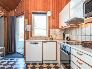 A compact kitchen with wooden walls, a window, a sink, a dishwasher, and a microwave.