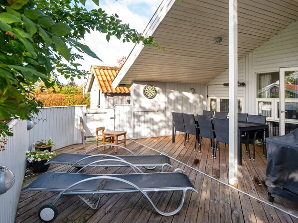 A covered outdoor patio with a table and chairs, a dartboard, and a wooden deck.