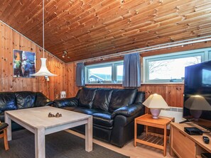 A cozy room with a wooden ceiling, a black leather sofa, a wooden coffee table, a small side table, and a television. - 4 Star Holiday Home in Juelsminde (Horsens)