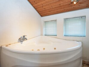 A large bathtub in a bathroom with wooden ceiling beams and two windows with blinds. - 4 Star Holiday Home in Juelsminde (Horsens)