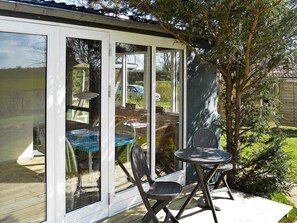 A covered patio with a table and chairs, a view of a car and greenery outside. - 4 Person Holiday Home in Broager (Broager)