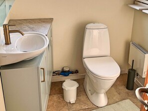 A compact bathroom with a white sink, a toilet, and a small trash bin.