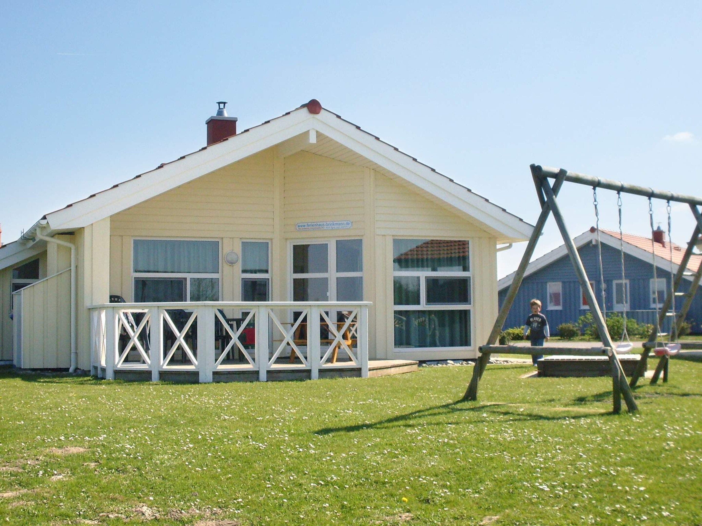 A building with a white exterior, a porch with white railings, and a swing set in the foreground.