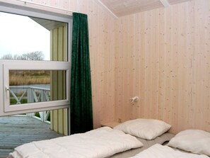 A room with a wooden floor, a bed with white bedding, a window with a view of a field, and a green curtain. - Holiday Home in Otterndorf (Otterndorf)