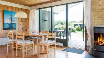 A wooden interior with a dining table, chairs, a fireplace, and a view through glass doors.