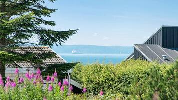 A coastal view with a ship in the distance, a building with a sloped roof, and lush greenery in the foreground.