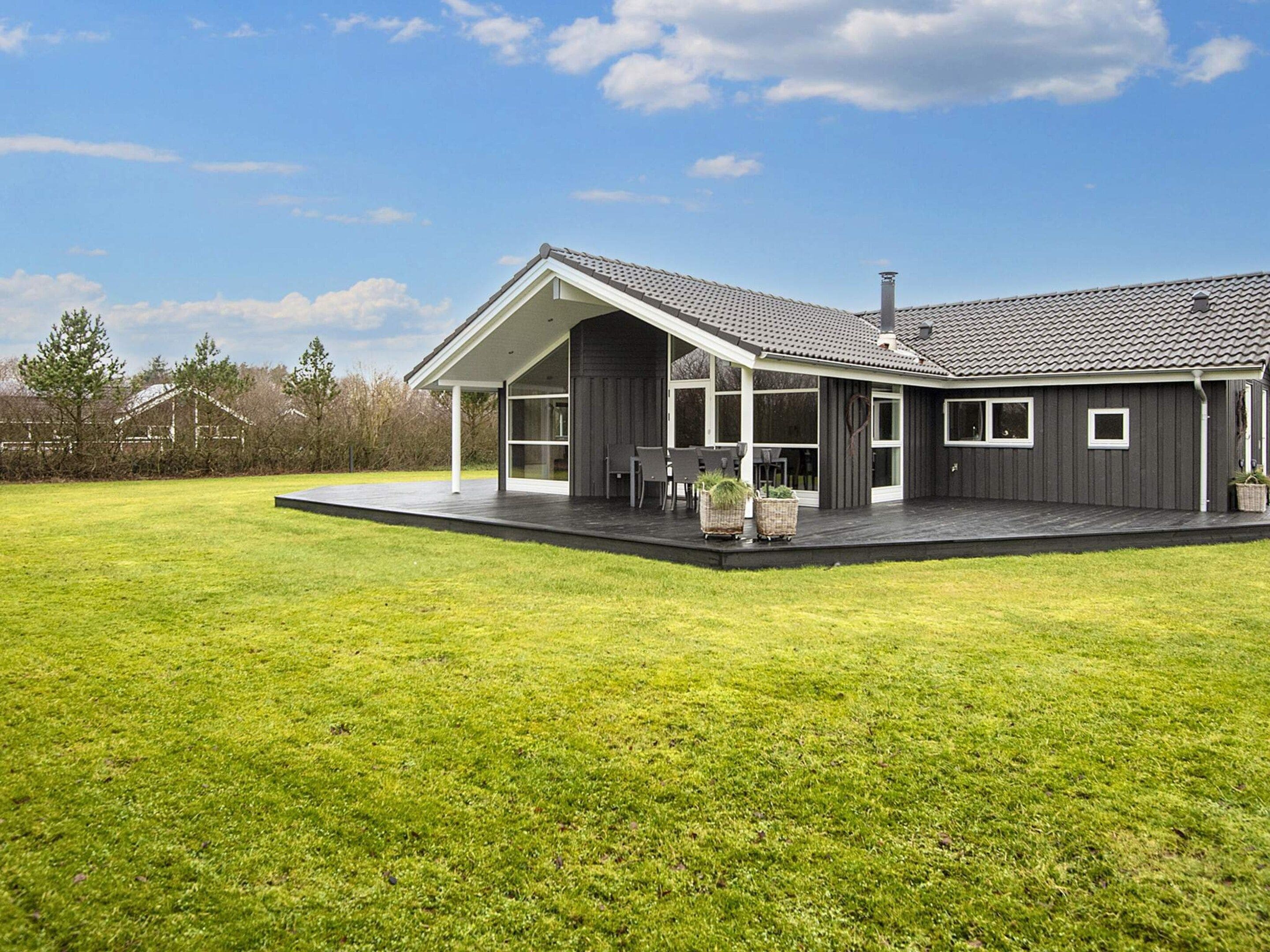Une maison moderne dotée d’un patio couvert, de grandes fenêtres et d’une pelouse bien entretenue.