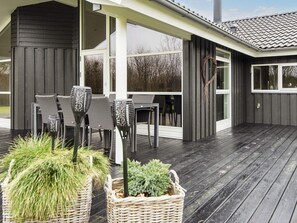 Un espace extérieur abrité, doté d’une terrasse en bois, de meubles en osier et de plantes en pot.