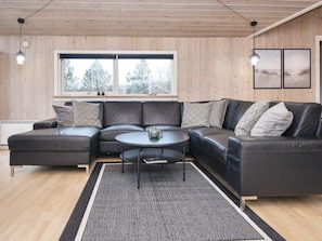 A modern living room with a sectional sofa, a coffee table, and a large window with a view of trees. - 5 Star Holiday Home in Hemmet (Hemmet)