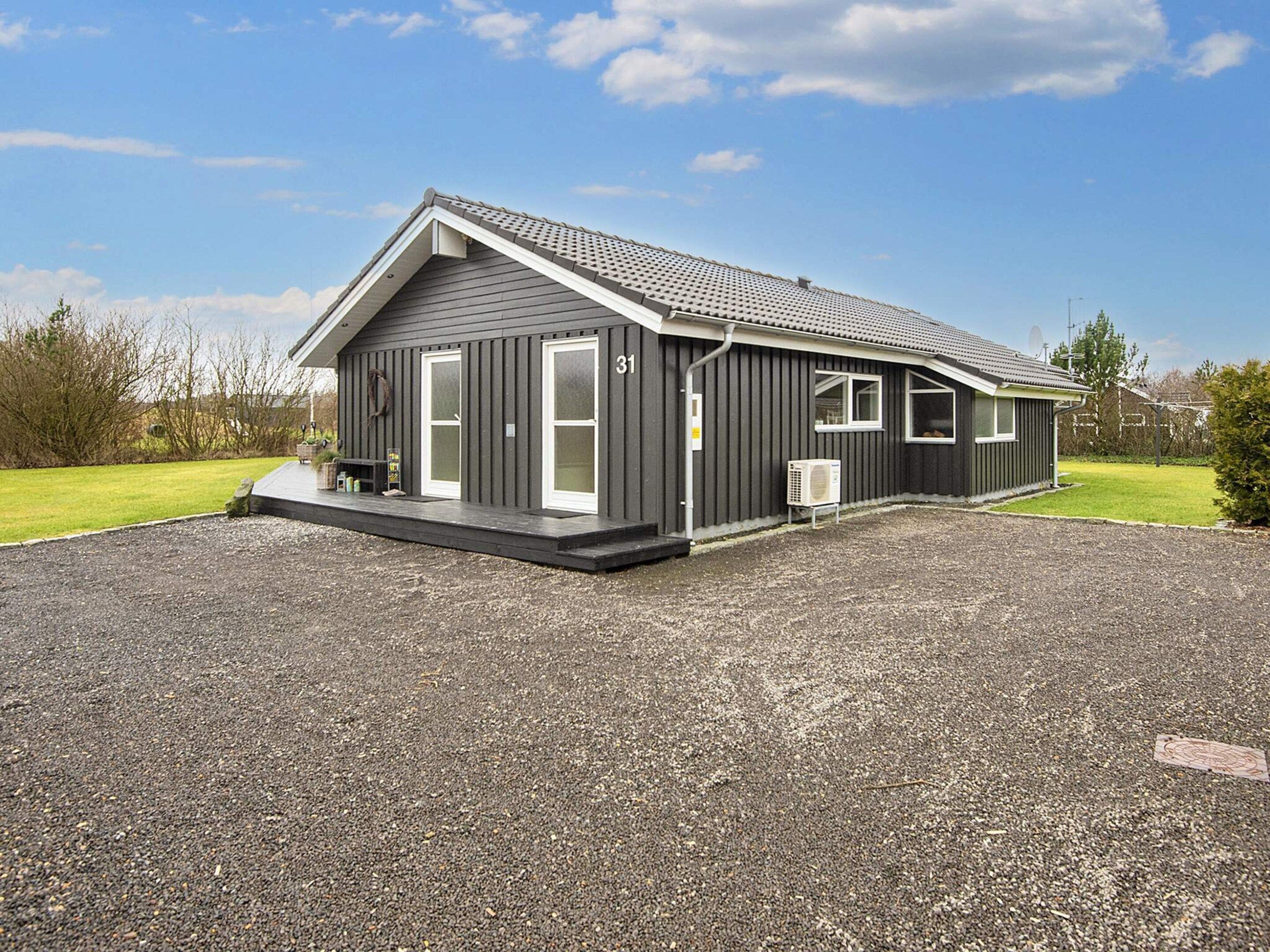 A single-story building with a dark exterior, a covered porch, and a gravel driveway.