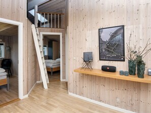Un intérieur moderne avec une chambre à coucher aménagée en mezzanine, un mur en bois orné d’une carte encadrée et un petit coin salon avec un haut-parleur et des vases décoratifs.