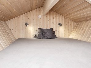 A bedroom with a sloped ceiling, wooden walls, a bed with grey bedding, and two wall-mounted lamps. - 5 Star Holiday Home in Hemmet (Hemmet)