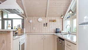 A modern kitchen with wooden cabinets, a dishwasher, and a stove. There are clocks on the wall and a window providing natural light. - 7 Person Holiday Home in Harboore-by Traum (Harboore)