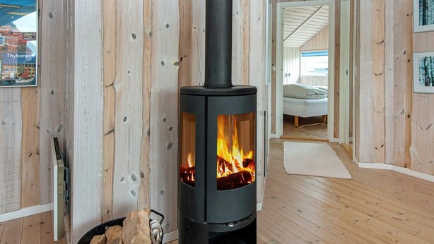 A cozy room with a wood-burning stove, wooden walls, and a bed in the background. - 7 Person Holiday Home in Harboore-by Traum (Harboore)