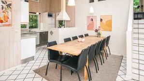A modern kitchen with wooden cabinets, a dining area with a wooden table and black chairs, and artwork on the walls.