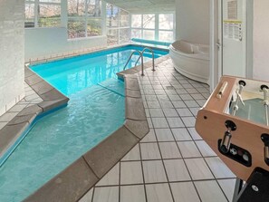 Una piscina con un jacuzzi y una tumbona, rodeada de suelo de baldosas y amplias ventanas.
