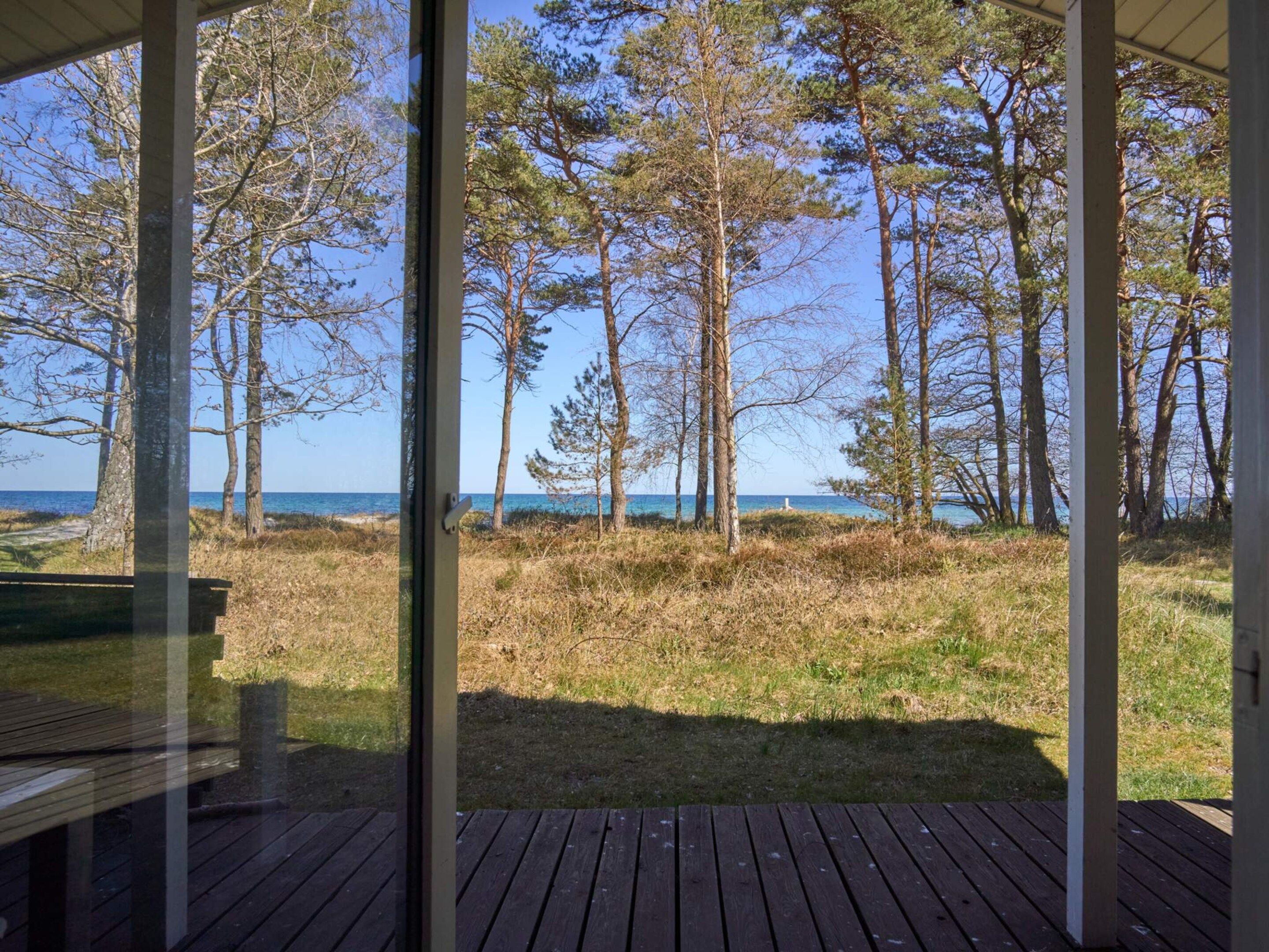 Un terrazzo in legno con una porta vetrata che dà su una zona erbosa con alberi e un corpo d'acqua.