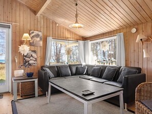 A cozy living room with a sectional sofa, a coffee table, and a view of the outdoors through large windows. - 4 Star Holiday Home in Nexo (Nexø)