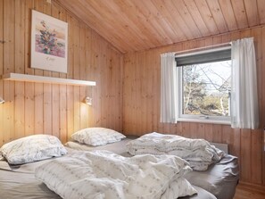 A room with wooden walls, a bed with floral bedding, a window with curtains, and a framed picture on the wall. - 4 Star Holiday Home in Nexo (Nexø)